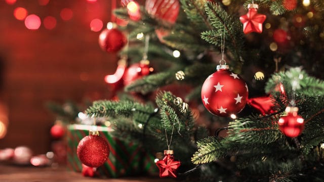 Weihnachtsbaum mit Dekorationen in der Nähe eines Kamins mit Lichtern